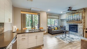 A modern kitchen with a large island, a stone fireplace, and a cozy seating area with a sofa and cushions. - 1820 The Seasons 1 Bedroom Condo (Keystone)