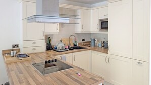 Una cocina moderna con armarios blancos, una campana extractora de acero inoxidable, un microondas y una encimera de madera.