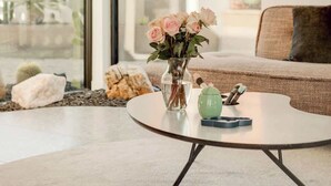 Una sala de estar moderna con una mesa redonda, un florero y vistas a un jardín a través de grandes ventanales.