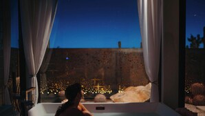 Una persona en una bañera con vista a un cielo estrellado y un espectáculo de luces decorativas en el exterior.