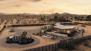 Un edificio moderno con techo plano, rodeado por un paisaje desértico con montañas al fondo.