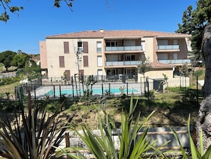 Un edificio de varios pisos con balcones, piscina y jardín vallado.