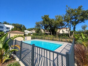 Ein rechteckiger Swimmingpool mit schwarzem Metallzaun, umgeben von Grünflächen und Wohngebäuden.