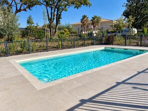 A rectangular swimming pool with clear blue water, surrounded by a tiled deck and a metal fence.