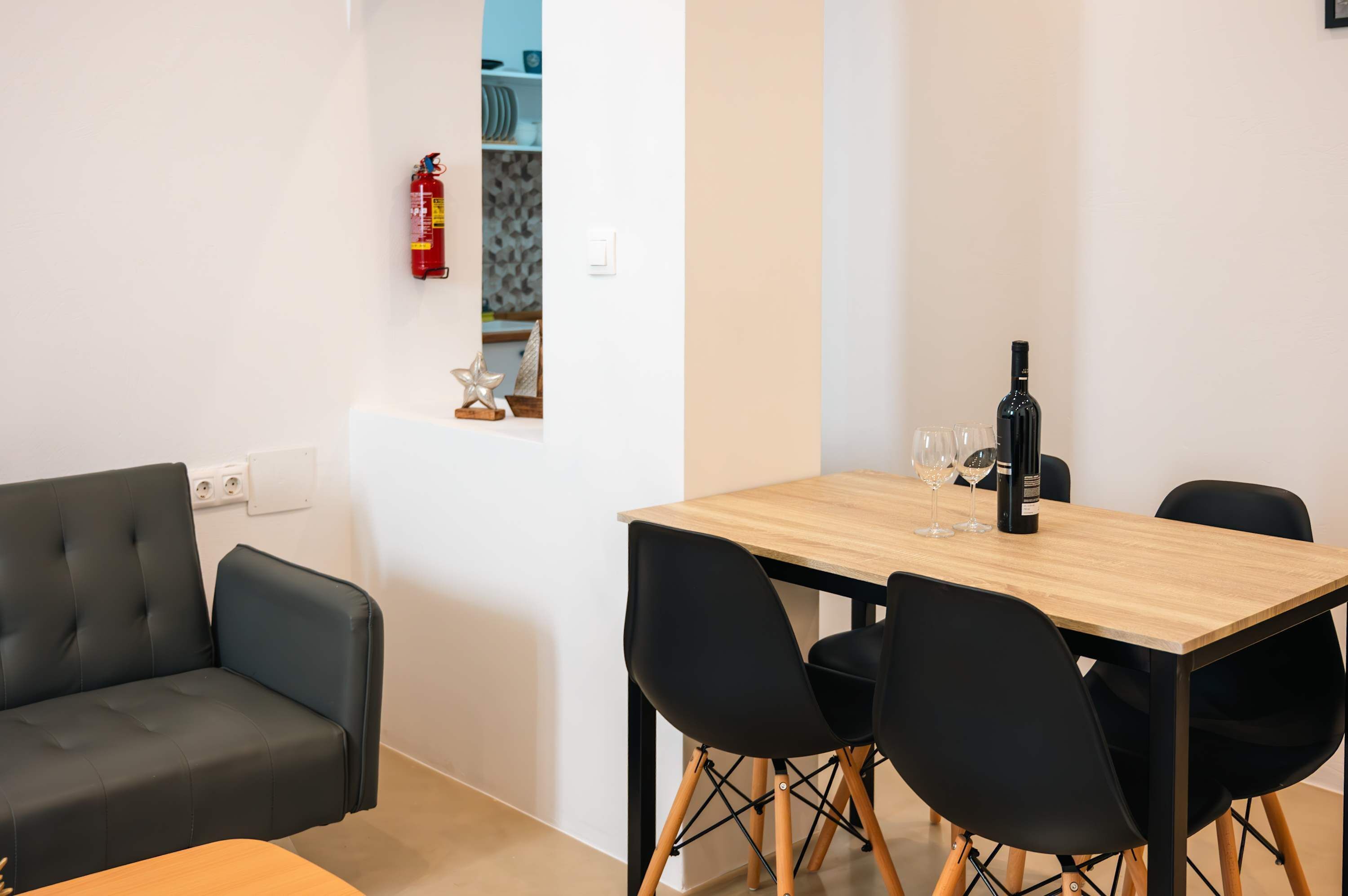 A modern living room with a sofa, a dining table with chairs, a wine bottle, and a fire extinguisher on the wall.