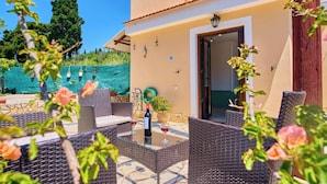 An outdoor patio with wicker furniture, a table with a bottle and glasses, and a door leading to the interior. - Villa Amarilda - Private Pool Garden in Corfu (Corfu)