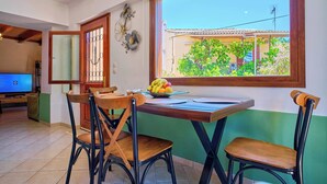 A dining area with a table, chairs, and a window with a view of greenery and a building. - Villa Amarilda - Private Pool Garden in Corfu (Corfu)