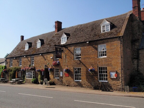 A traditional stone building with multiple windows, a signboard, and outdoor seating.