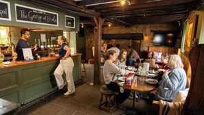 A bar area with a counter, stools, and a stone wall backdrop. - The George Inn (Lower Brailes)