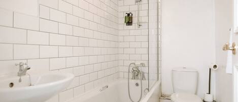 A bathroom with white tiled walls, a bathtub, a sink, and a toilet.