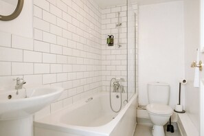 A bathroom with white tiled walls, a bathtub, a sink, and a toilet.