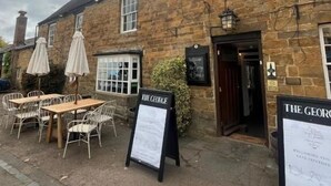 A stone building with outdoor seating and a sign reading "The George". - The George Inn (Lower Brailes)