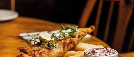 A plate of fish and chips with lemon wedges and a side of coleslaw on a wooden table.