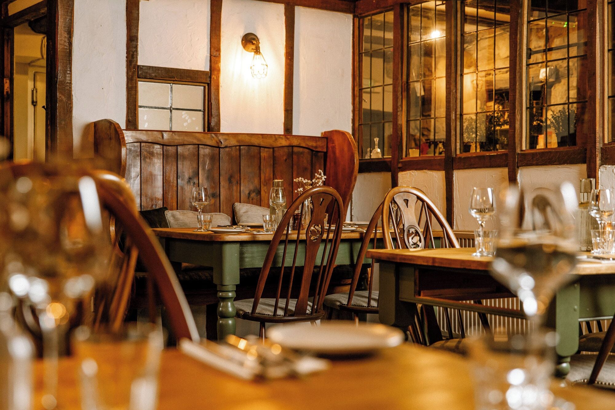 A restaurant interior with wooden furniture, tables set for dining, and a large window with a view.