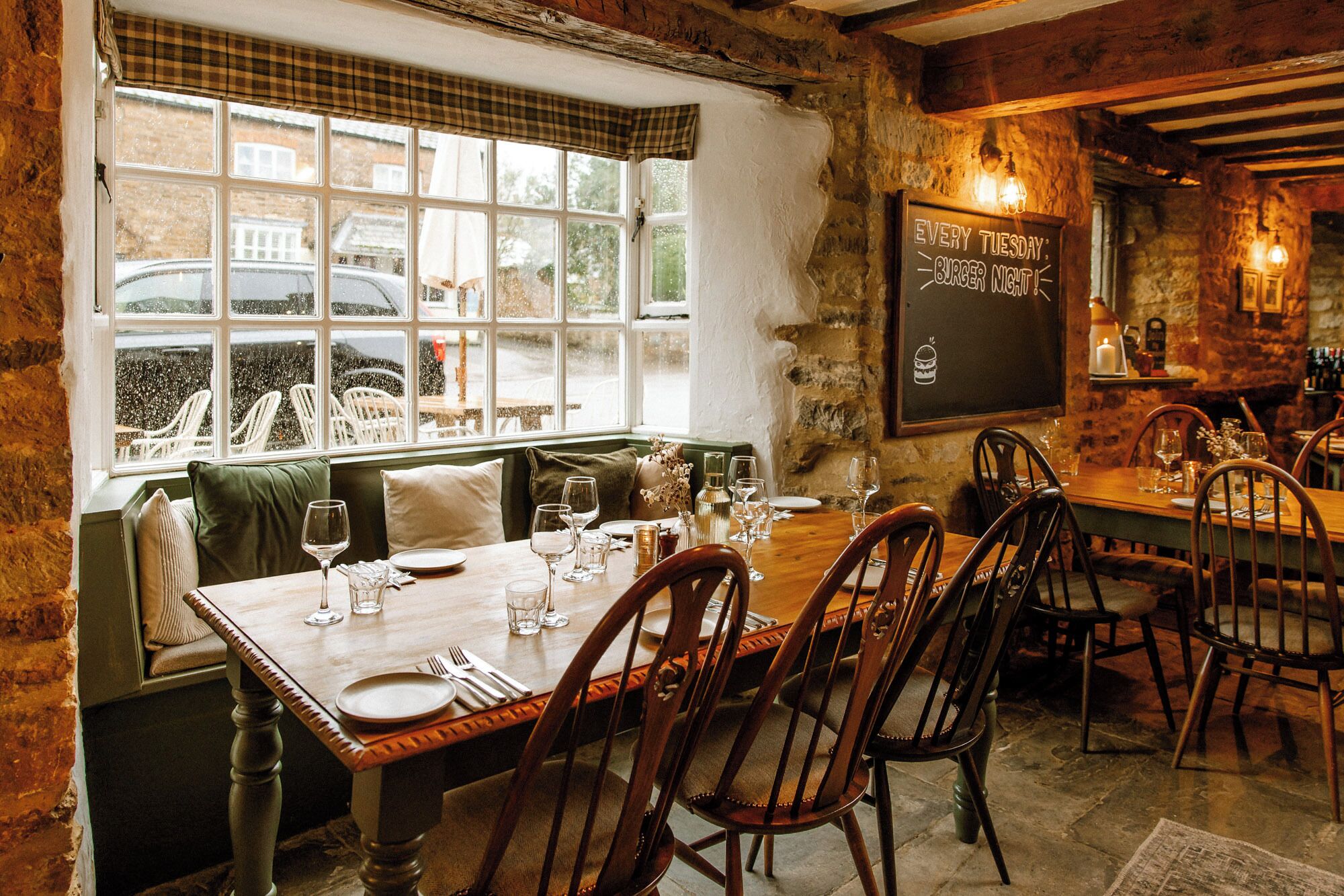 Un restaurante acogedor con interior de madera, un menú en la pizarra y vista a coches estacionados afuera.