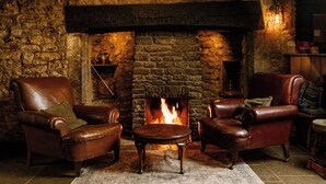 A cozy room with a stone fireplace, leather armchairs, a small round table, and a rug on the floor. - The George Inn (Lower Brailes)