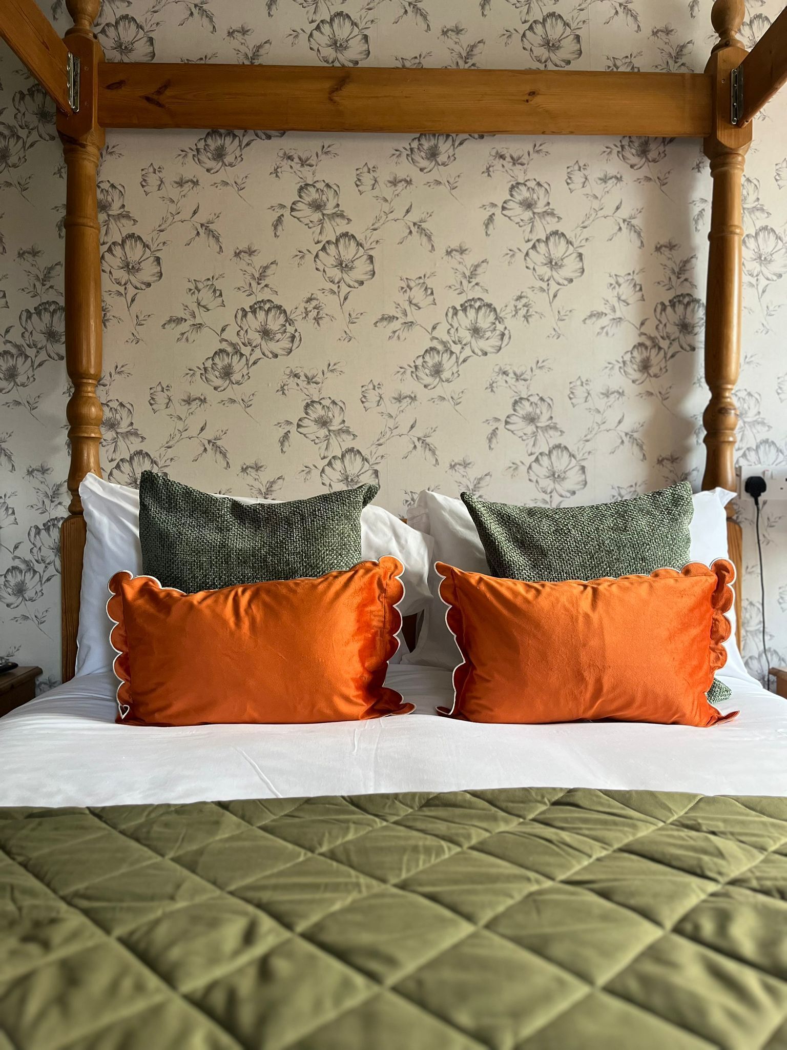 Een hemelbed met een groene sprei, twee oranje kussens en een gebreide groene deken.