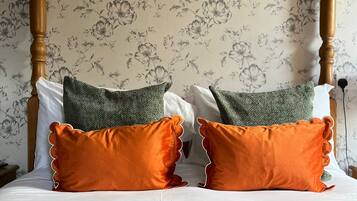 Een hemelbed met een groene sprei, twee oranje kussens en een gebreide groene deken.