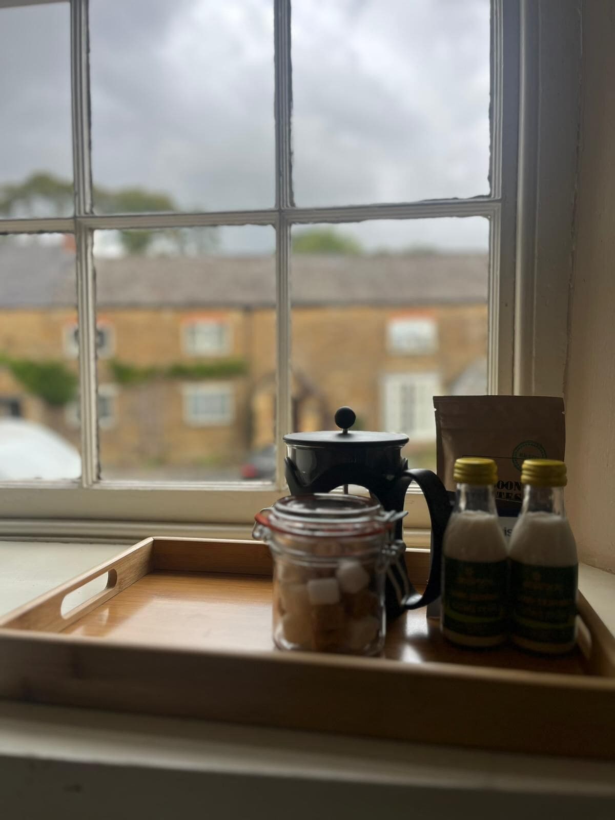 A window with a view of buildings and a tray with a jar, a pot, and two bottles.