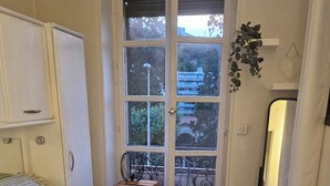 A bedroom with a bed, a wardrobe, a small table, a window with a view, and a mirror. - Apartment facing the Royat thermal baths (Royat)