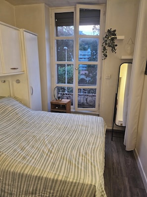 A bedroom with a bed, a wardrobe, a small table, a window with a view, and a mirror.
