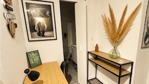 A room with a wooden desk, a framed picture, a vase with pampas grass, and a door leading to a bathroom. - Apartment facing the Royat thermal baths (Royat)