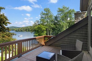 Une terrasse dotée de meubles en osier, donnant sur un lac et entourée d’arbres et de collines.