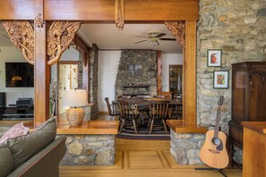 Un coin repas aux murs de pierre, avec une table et des chaises en bois, une guitare et un ventilateur de plafond.