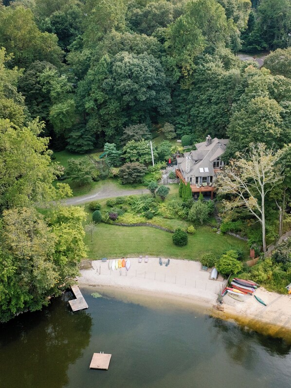 An aerial view of a lakeside property with a dock, a house with a stone facade, and lush greenery surrounding the area.