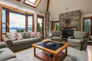 Un salon chaleureux avec une cheminée en pierre, de grandes fenêtres et une vue sur un lac.