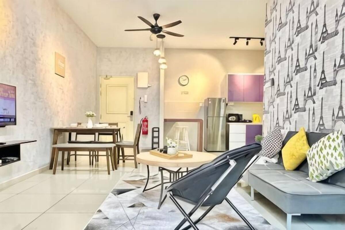 A modern living room with a sofa, a dining table, a TV, and a kitchen area in the background.