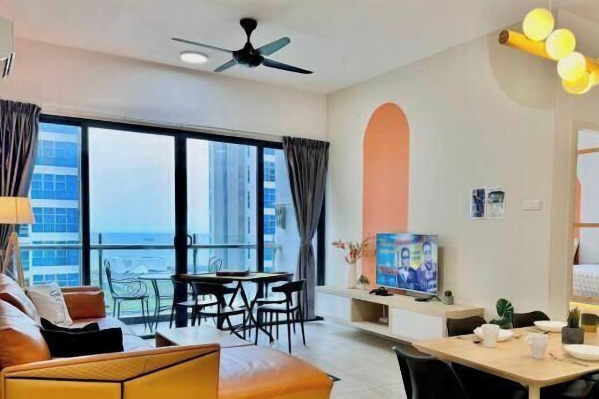 A modern living room with a sofa, dining table, and chairs, a ceiling fan, and a TV on a stand.