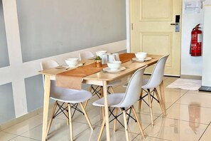 Un comedor con una mesa larga, sillas blancas y un extintor de incendios en la pared.