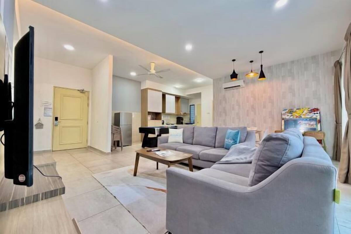 A modern living room with a sofa, coffee table, and TV. There is a kitchen in the background.