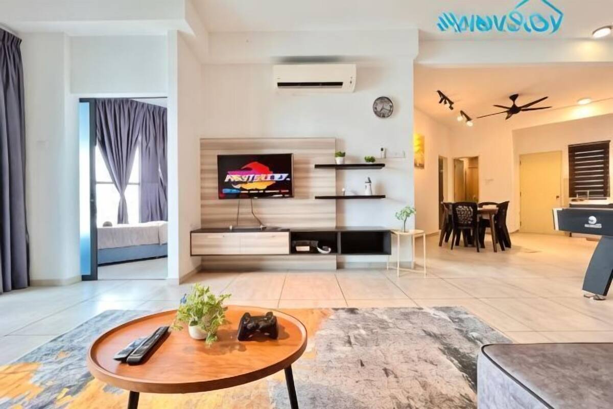 A modern living room with a flat-screen TV, a gaming console, and a dining area with a table and chairs.
