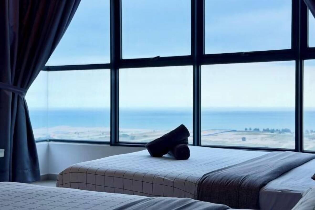 A hotel room with a large window, a bed with a pillow, and a view of the sea.