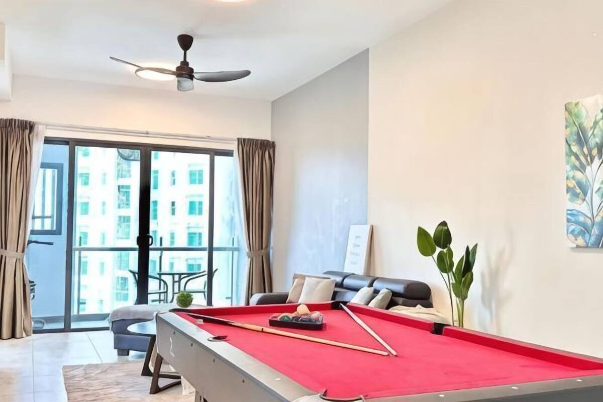 A modern hotel room with a pool table, a ceiling fan, a balcony with a view of buildings, and a potted plant.