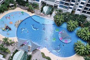 Una amplia piscina al aire libre con diseños de delfines, rodeada de palmeras y un complejo de edificios.