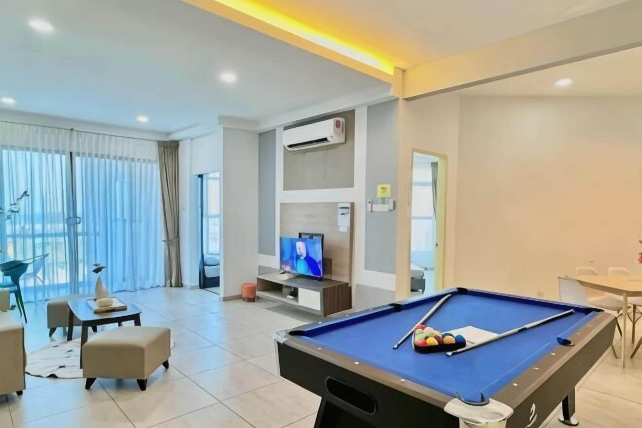 A pool table in a modern room with a television, seating area, and a large window.