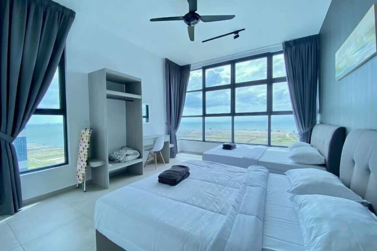A modern hotel room with a large bed, a desk, and a view of the ocean.