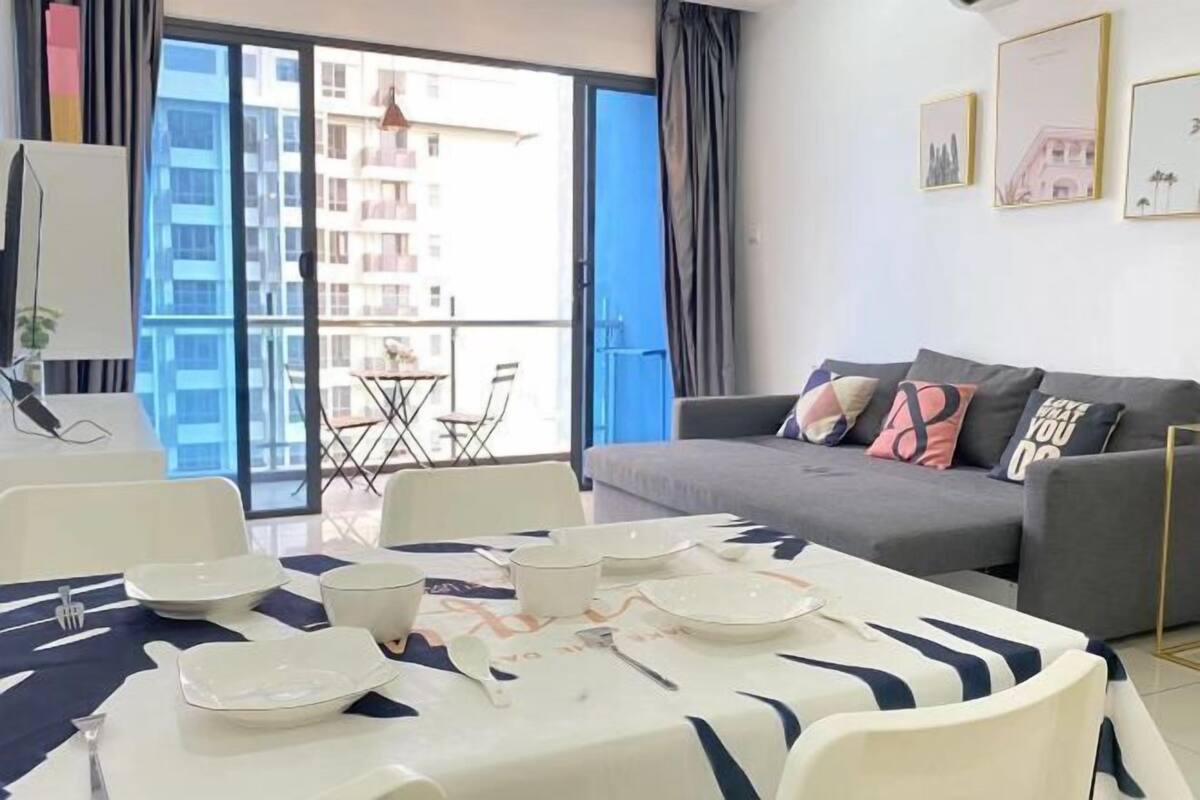 A modern living room with a dining area, a grey sofa, and a balcony with a view of buildings.