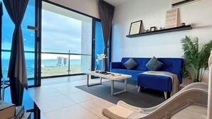 Un salon moderne avec un canapé bleu, une table basse et une vue sur le paysage urbain grâce à de grandes fenêtres.