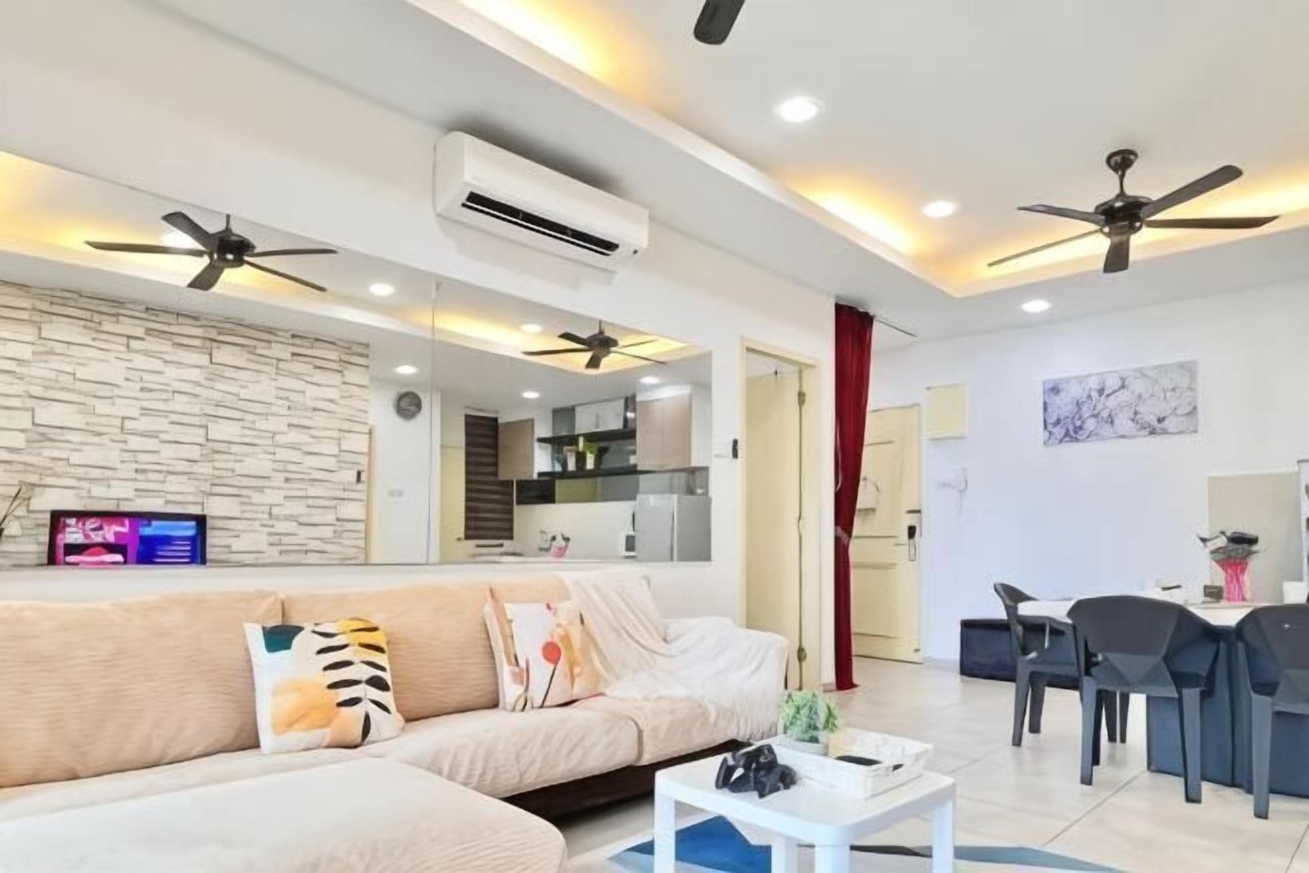 A modern living room with a sofa, a coffee table, and a dining area with chairs and a table. There are ceiling fans, recessed lighting, and an air conditioning unit.