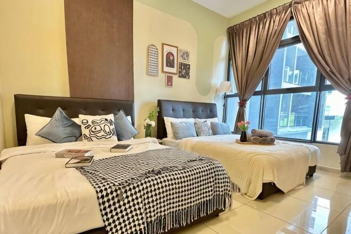A hotel room with two beds, a large window with curtains, a nightstand, and a vase with flowers.