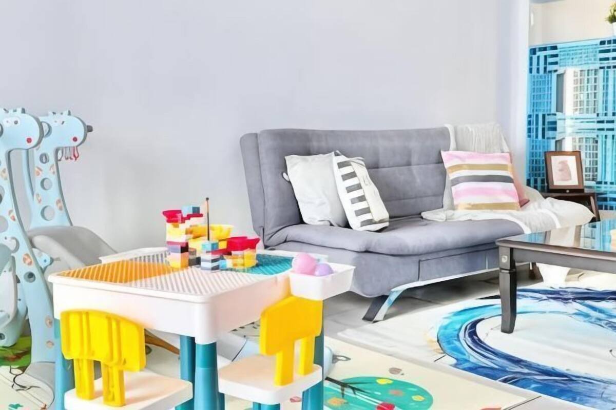 A living room with a grey sofa, colorful pillows, a small table, and a children's play area with a giraffe-shaped toy.
