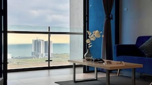 Un salon moderne avec une grande fenêtre, un canapé bleu, une petite table avec un vase et une vue sur un chantier de construction.