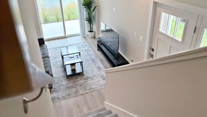 A spacious living area with a large window, a glass coffee table, a sofa, and a potted plant. - 4BR Home Near Naperville! Parking + Pickleball (Warrenville)