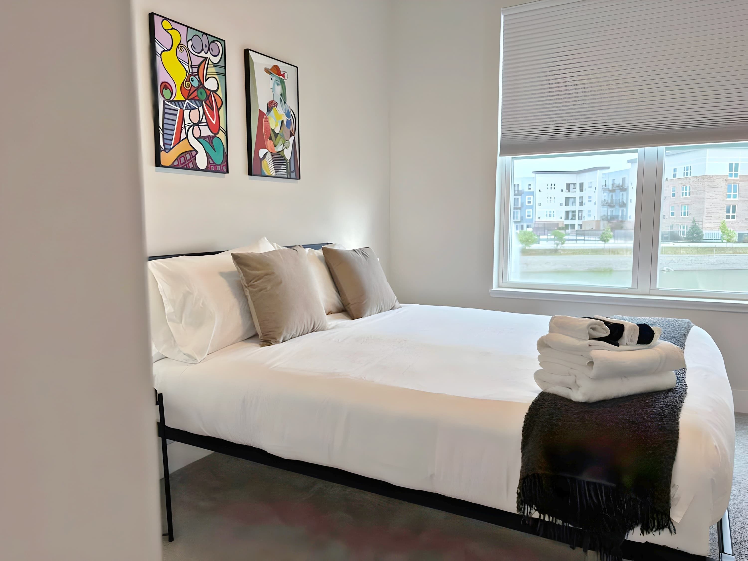 Une chambre à coucher moderne avec un grand lit, du linge de lit blanc et deux tableaux abstraits accrochés au mur.
