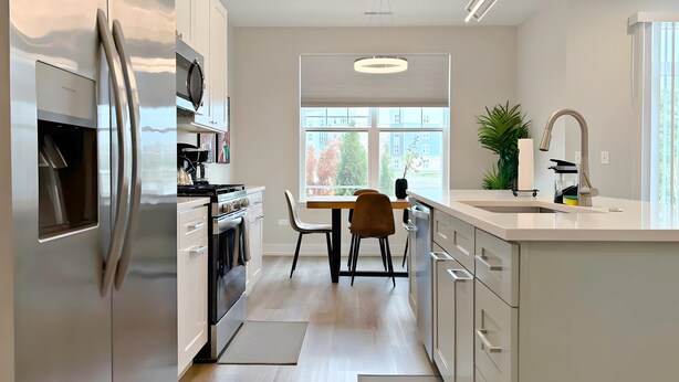 A modern kitchen with white cabinetry, stainless steel appliances, a dining area with a table and chairs, and a large window providing a view of the outside. - 4BR Home Near Naperville! Parking + Pickleball (Warrenville)