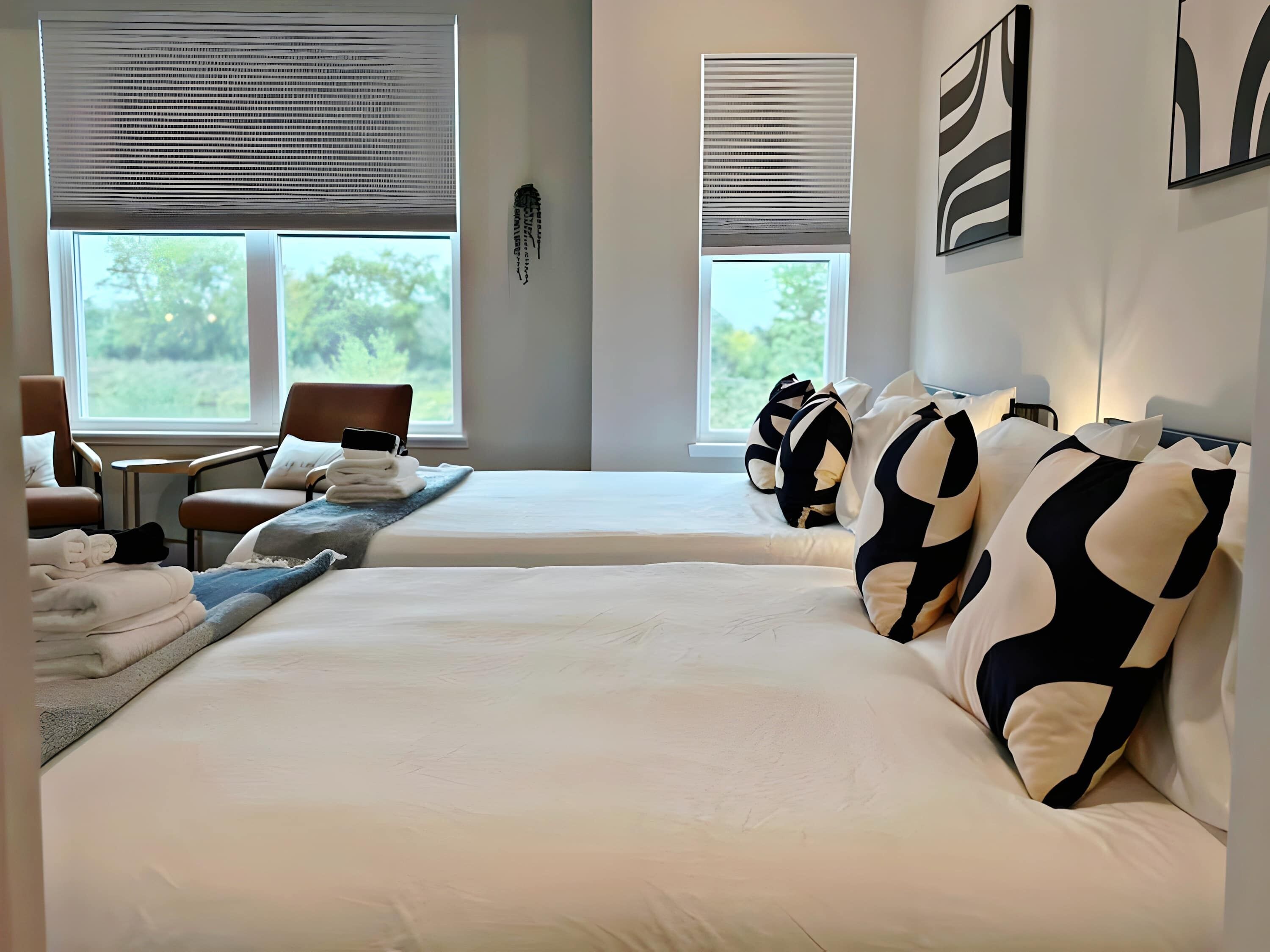 Une chambre d’hôtel avec deux lits, un coin salon avec des fauteuils et des œuvres d’art aux murs.